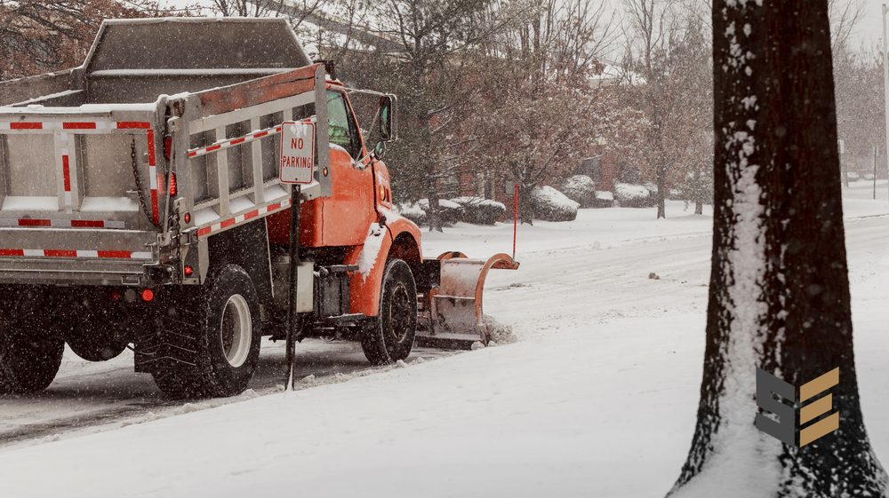 Plow and material truck servicing a snowy commercial street